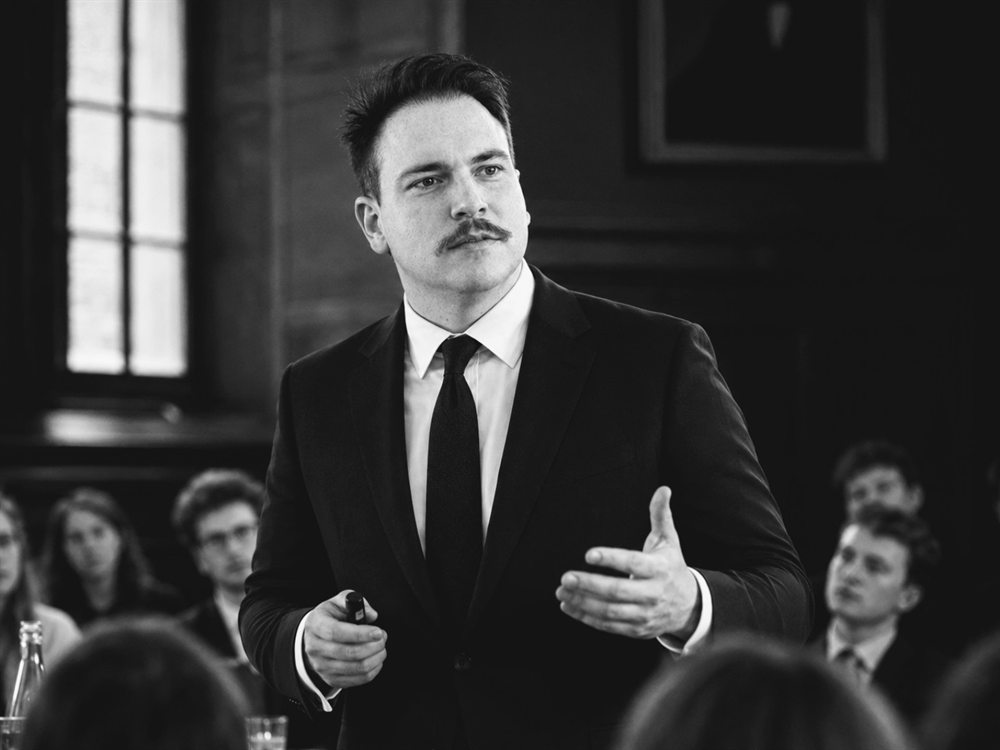 Lawrence Jell speaking to an audience in a panelled hall.